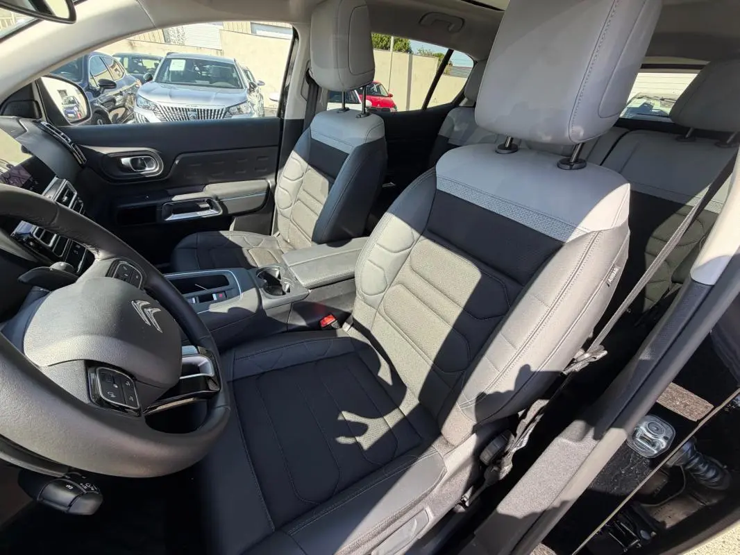 Vue intérieure côté conducteur du Citroën C5 Aircross hybride 2024 noir, avec sièges bi-ton gris et noir et volant multifonction.