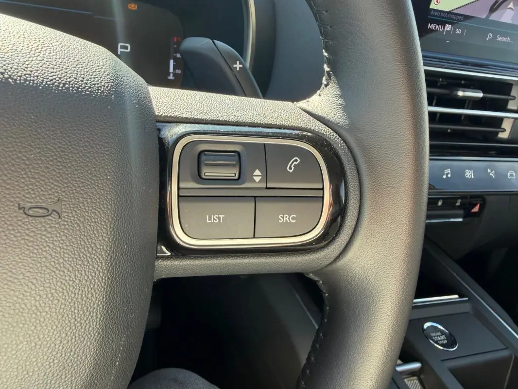 Gros plan sur les commandes au volant du Citroën C5 Aircross Hybride 2024, intérieur noir avec boutons fonction téléphone et liste.