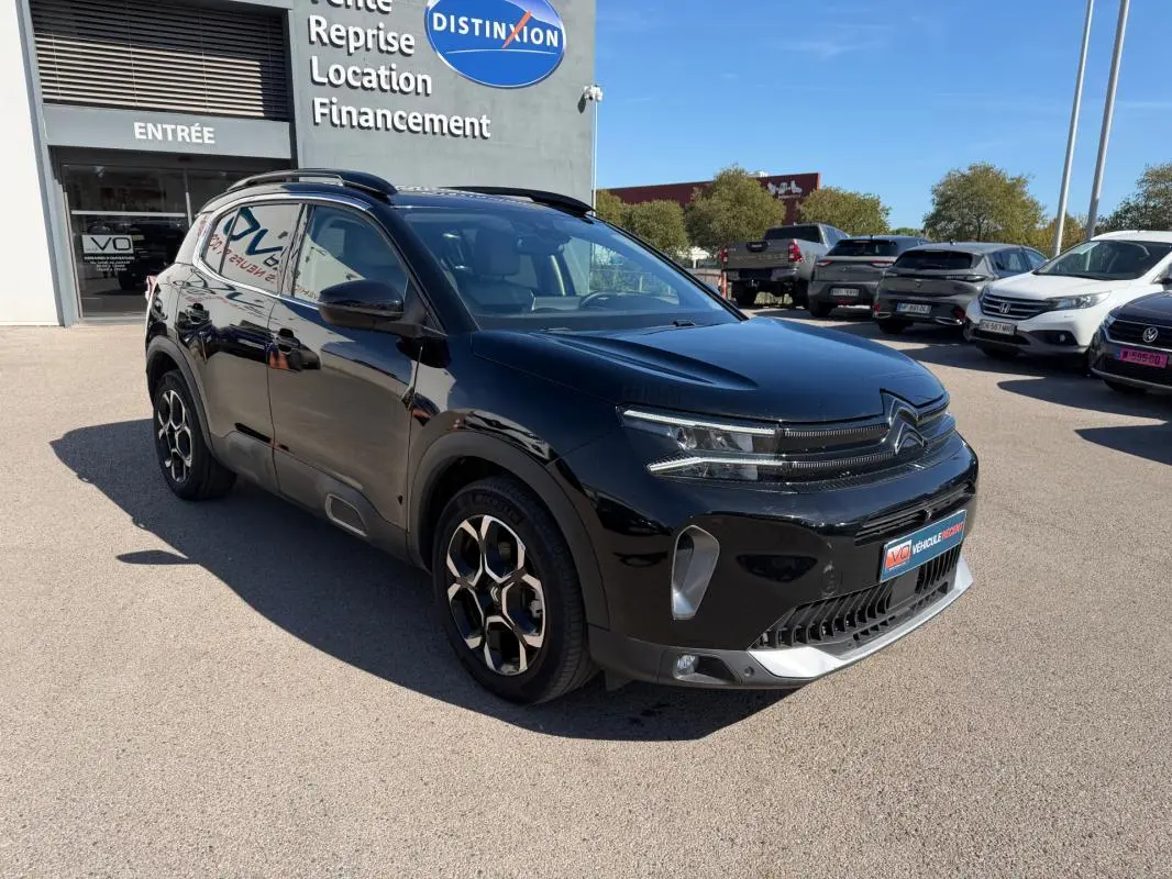 Citroën C5 Aircross Hybride noir vue 3/4 avant droit, avec jantes distinctives et calandre moderne, stationné devant un concessionnaire.