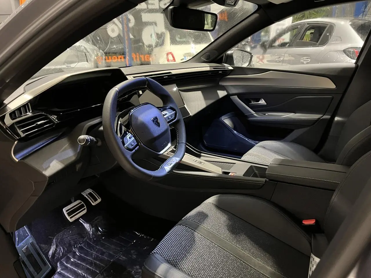 Intérieur avant droit de la Peugeot 308 2024, volant cuir, sellerie tri-matières et planche de bord moderne noire.