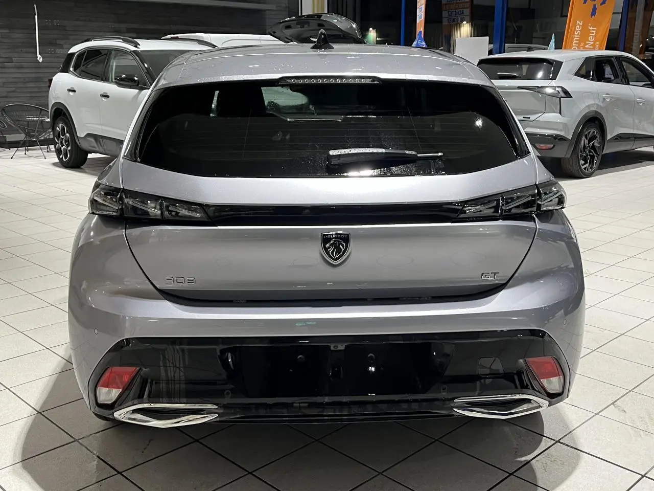 Vue arrière d'une Peugeot 308 GT gris Artense avec feux arrière en bandeau noir brillant et double sortie d'échappement chromée.