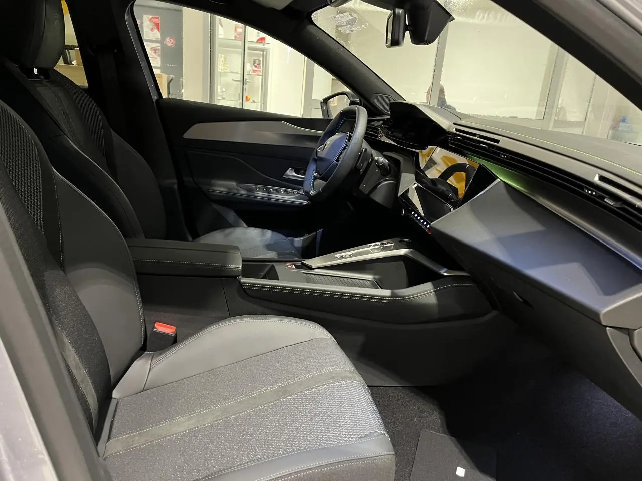 Intérieur avant droit de la Peugeot 308 GT 2024 avec sellerie tissu/TEP gris et planche de bord moderne noire.