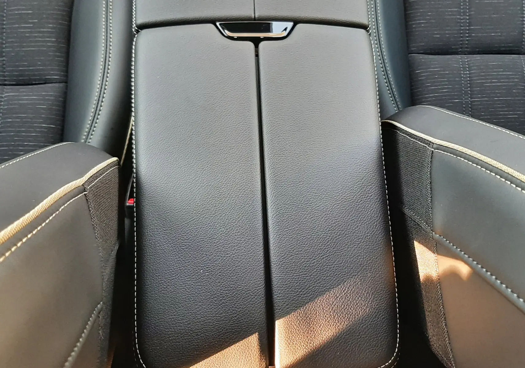 Gros plan sur la console centrale noire en cuir avec surpiqûres blanches, entre les sièges avant du Renault Austral 2025.