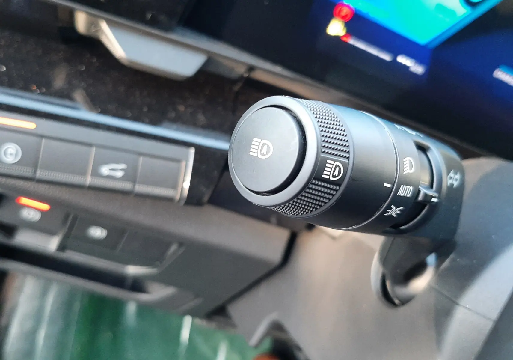 Gros plan sur la commande des phares du Renault Austral E-Tech blanc nacré, avec tableau de bord numérique en arrière-plan.