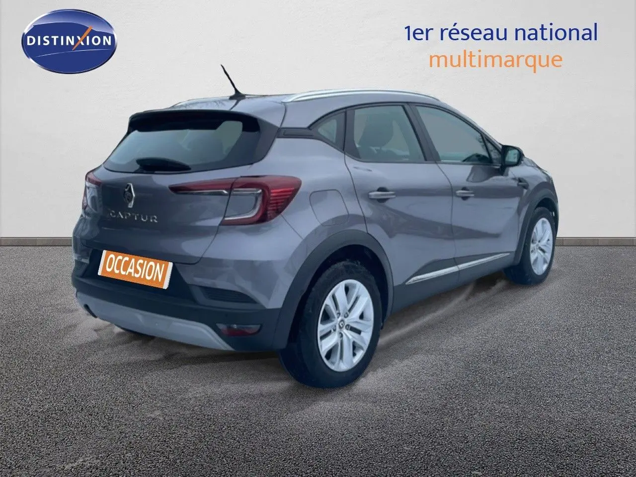 Vue 3/4 arrière droite d’un Renault Captur gris Cassiopée métal avec jantes blanches et badge arrière visible.