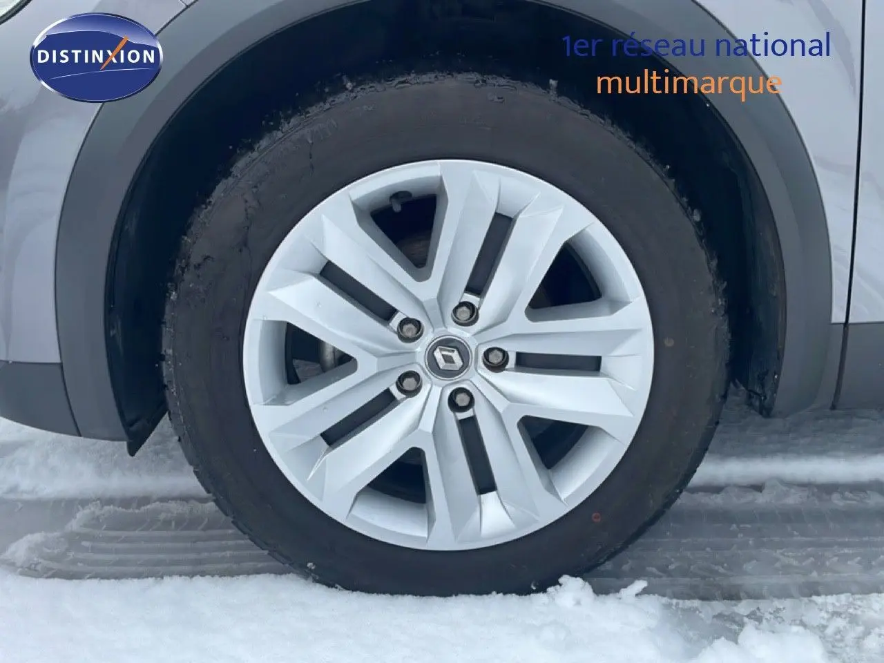 Gros plan sur la roue avant gauche du Renault Captur gris Cassiopée métal, avec jante alliage et neige au sol.