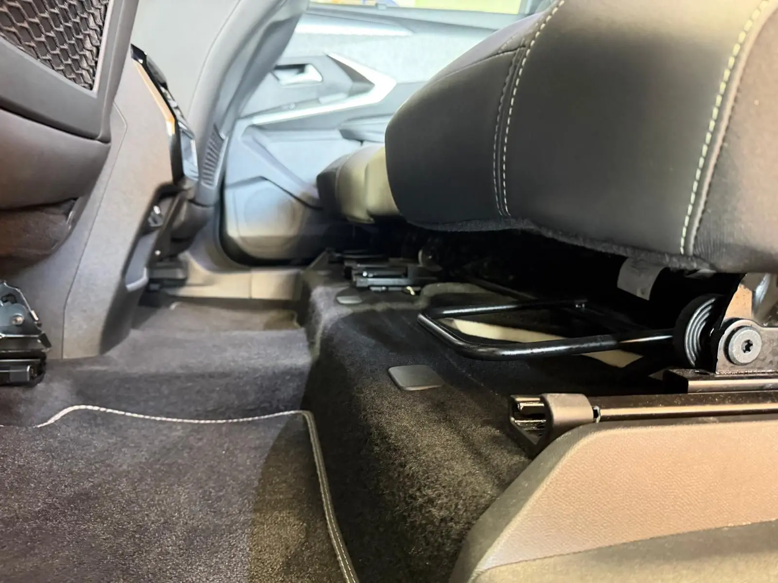 Vue en contre-plongée sous les sièges arrière du Peugeot 5008 Hybrid 145 GT, montrant la moquette noire et les rails de fixation.