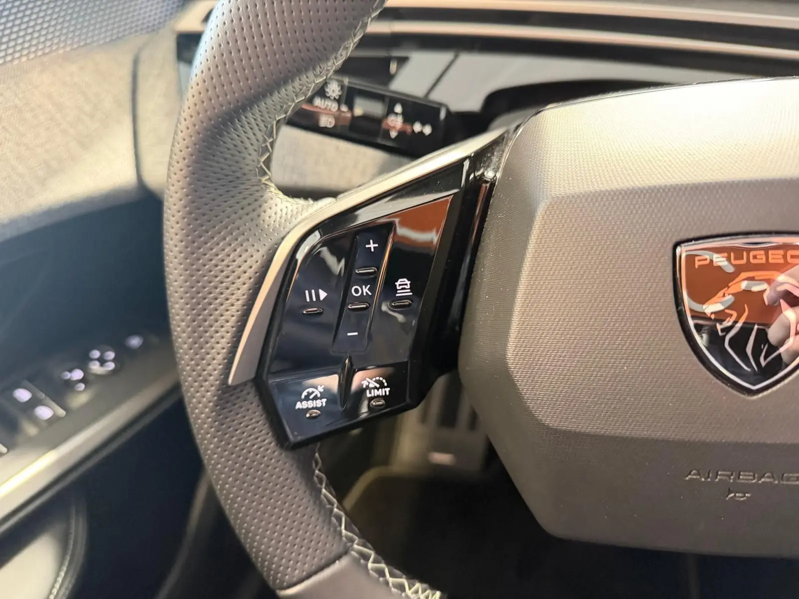 Gros plan sur le volant perforé du Peugeot 5008 Hybrid 145 GT avec commandes d’assistance et logo lion orange.