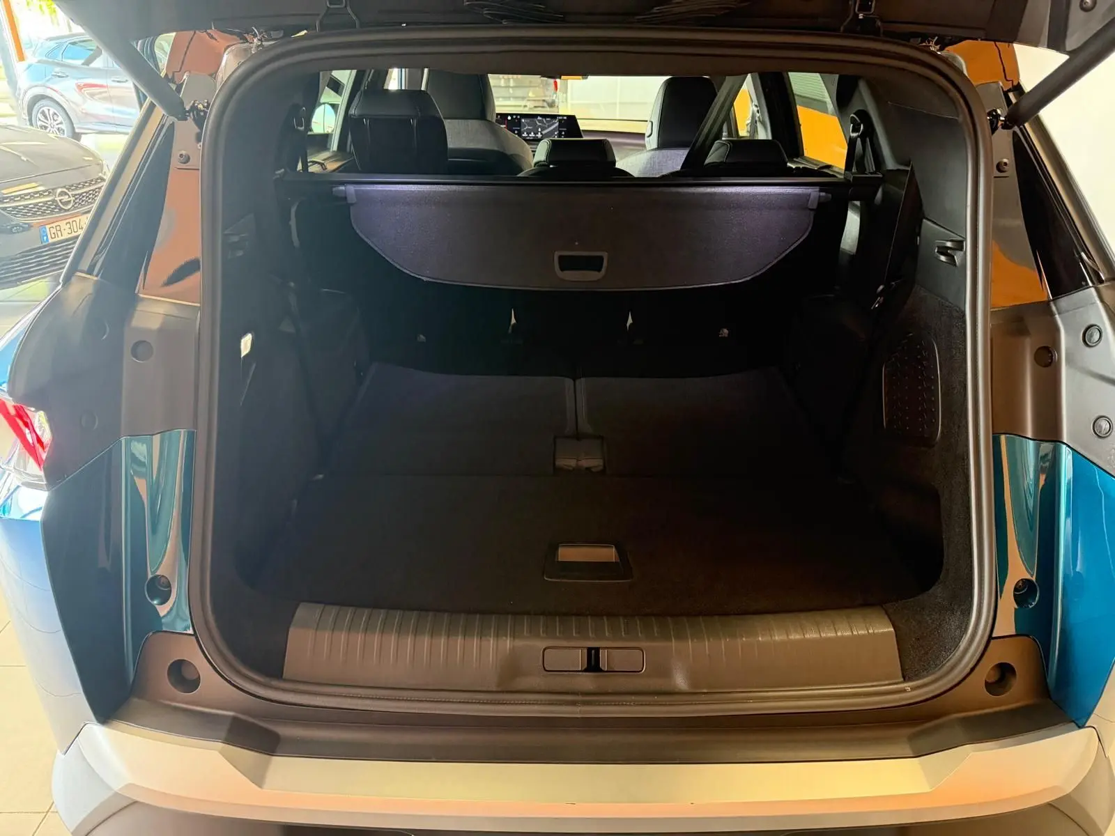 Coffre ouvert vu de l'arrière du Peugeot 5008 Hybrid 145 bleu obsession avec toit noir dans un showroom.