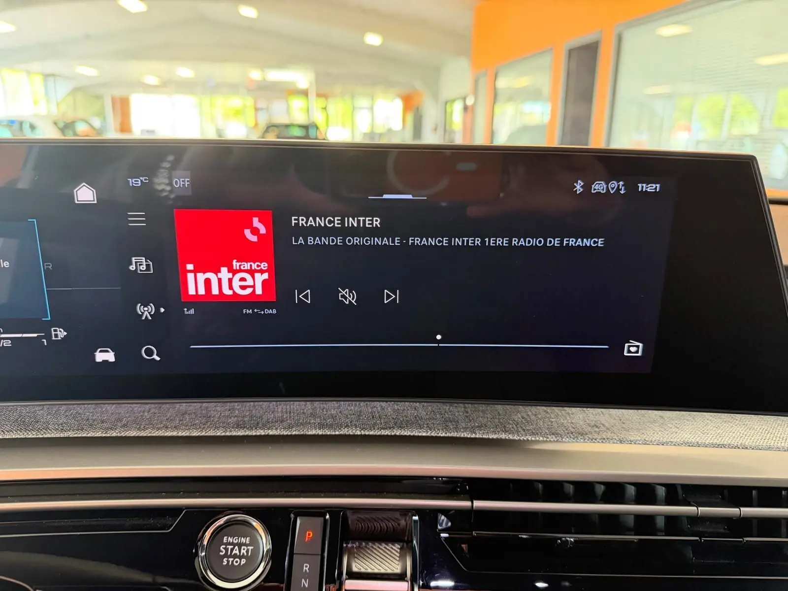 Vue rapprochée de l'écran HD 21’’ du Peugeot 5008 Hybrid 145 GT affichant France Inter, avec bouton start/stop en dessous.