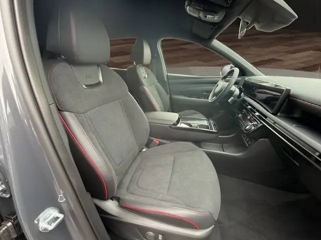 Vue intérieure côté conducteur du Hyundai Tucson gris foncé 2026, sièges en tissu noir avec surpiqûres rouges et tableau de bord moderne.