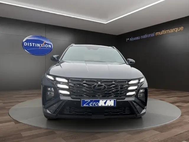 Vue frontale d'un Hyundai Tucson gris foncé 2026 avec calandre noire et feux LED distinctifs allumés.