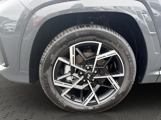 Gros plan sur la roue avant gauche du Hyundai Tucson gris foncé, mettant en valeur la jante alliage au design géométrique.