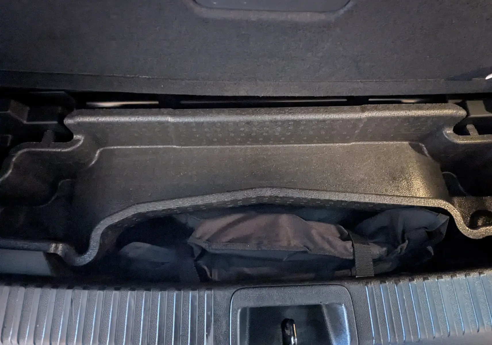 Vue rapprochée du rangement sous le plancher du coffre du Renault Espace VI noir Étoile, avec une housse noire visible.
