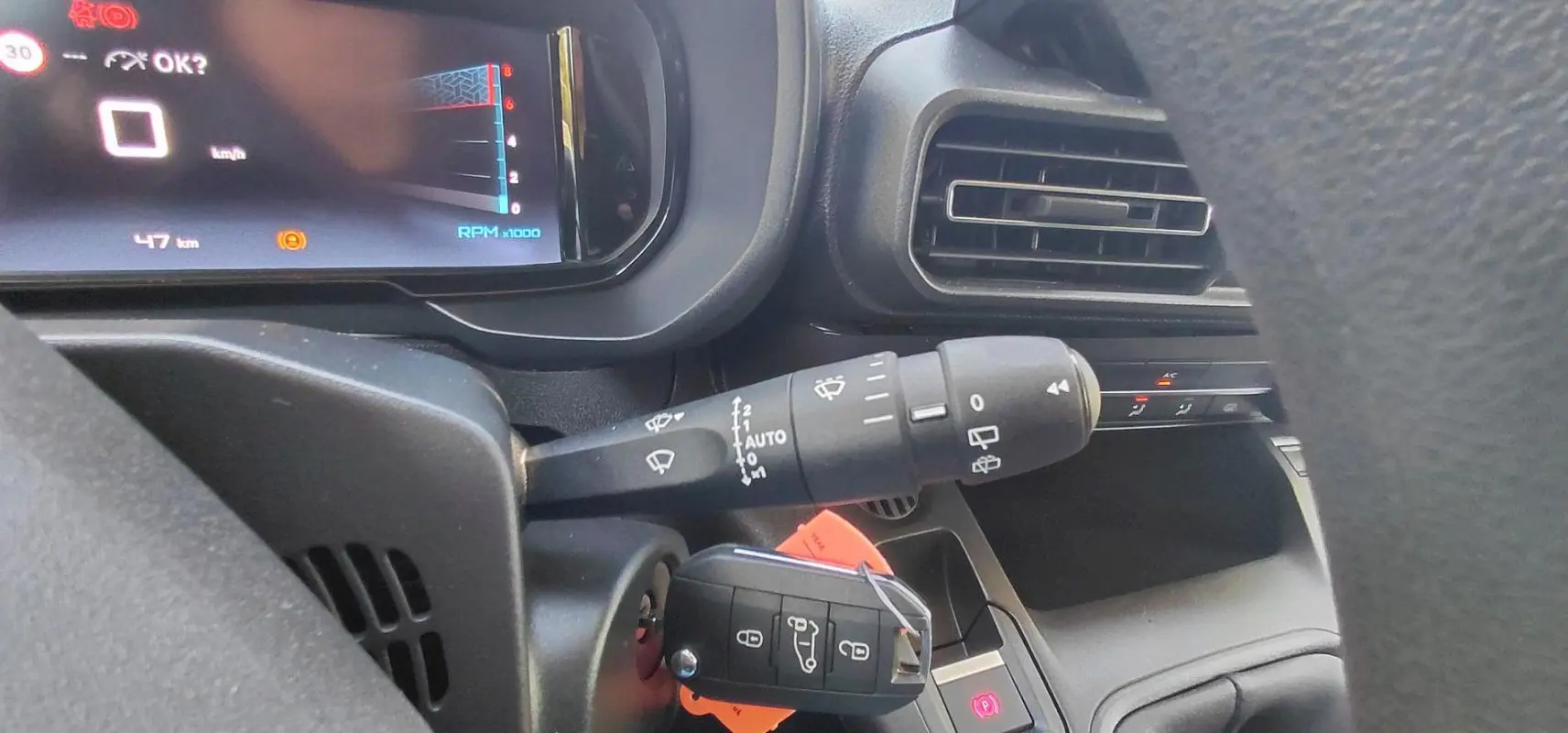 Gros plan sur le tableau de bord et la clé de contact du Citroën Berlingo 2025, avec commandes de phares et ventilation visibles.