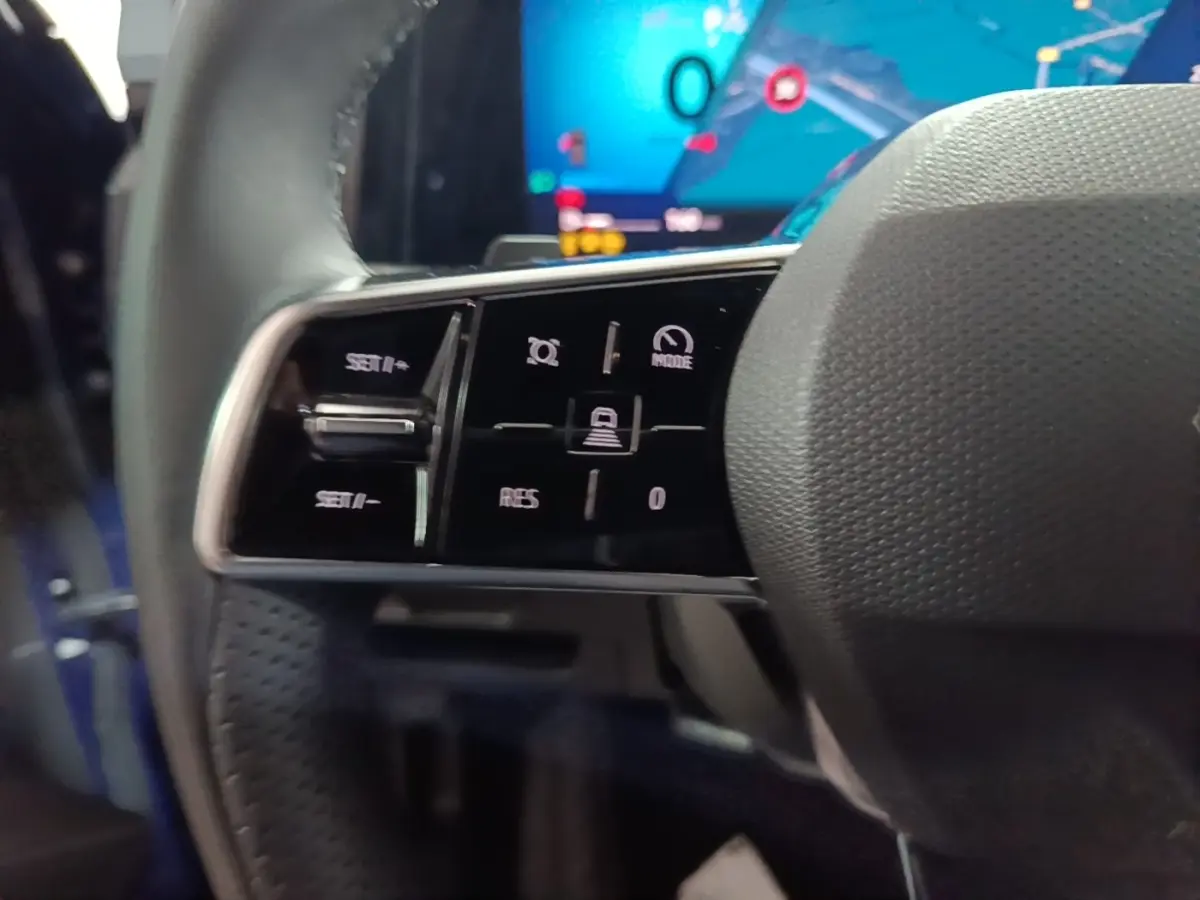 Gros plan sur les commandes du volant cuir côté gauche du Renault Austral bleu, avec écran numérique en arrière-plan.