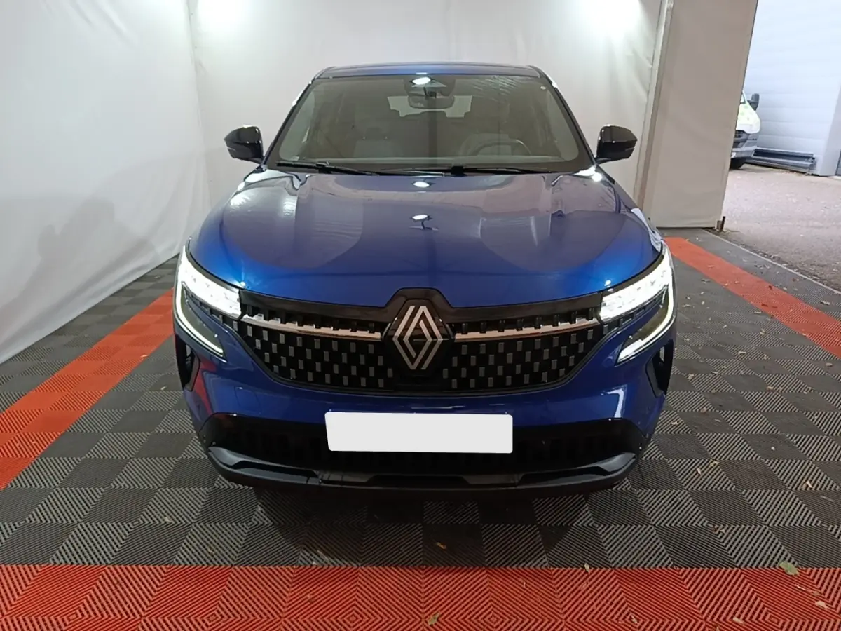 Vue frontale d'un Renault Austral bleu 2024 avec calandre noire et phares LED allumés dans un espace fermé.