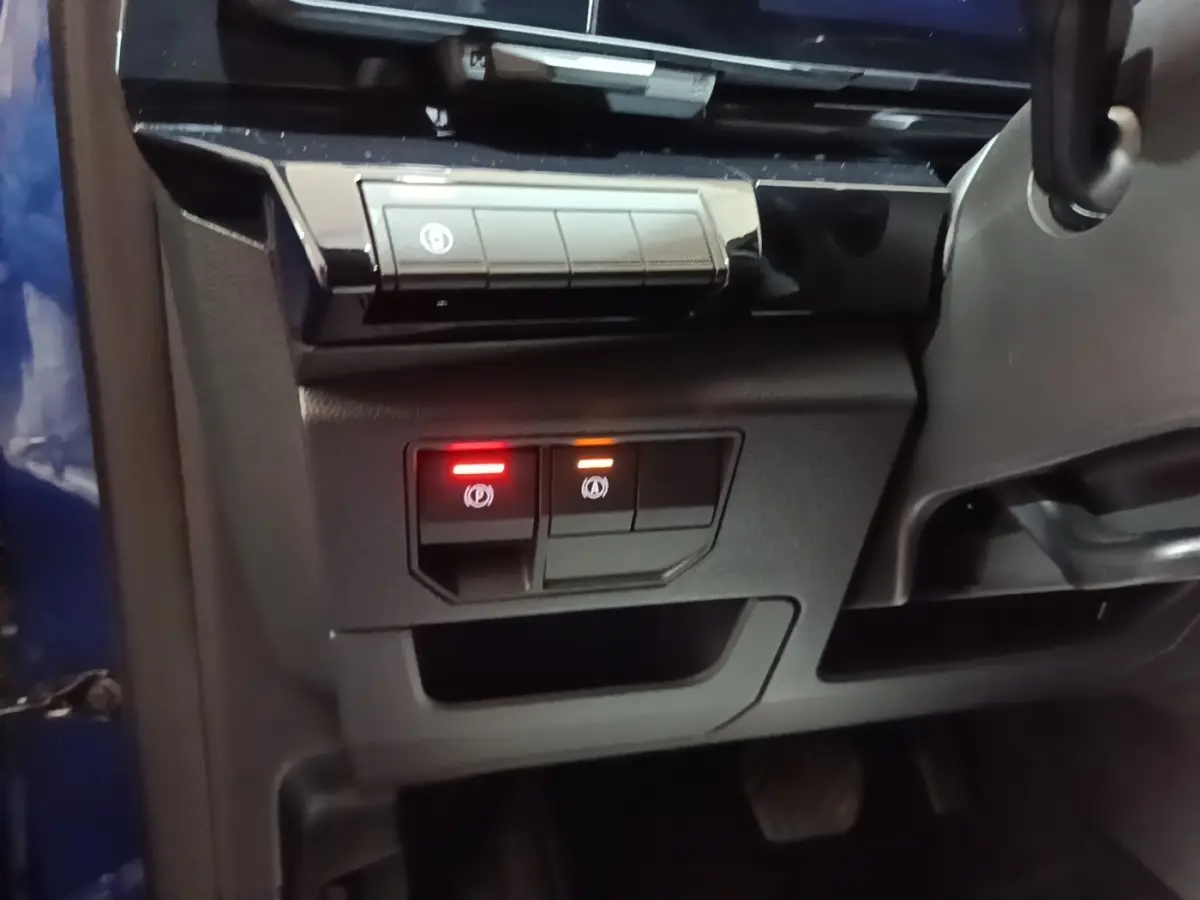 Détail intérieur côté gauche du tableau de bord du Renault Austral bleu, avec boutons de frein à main électrique éclairés.