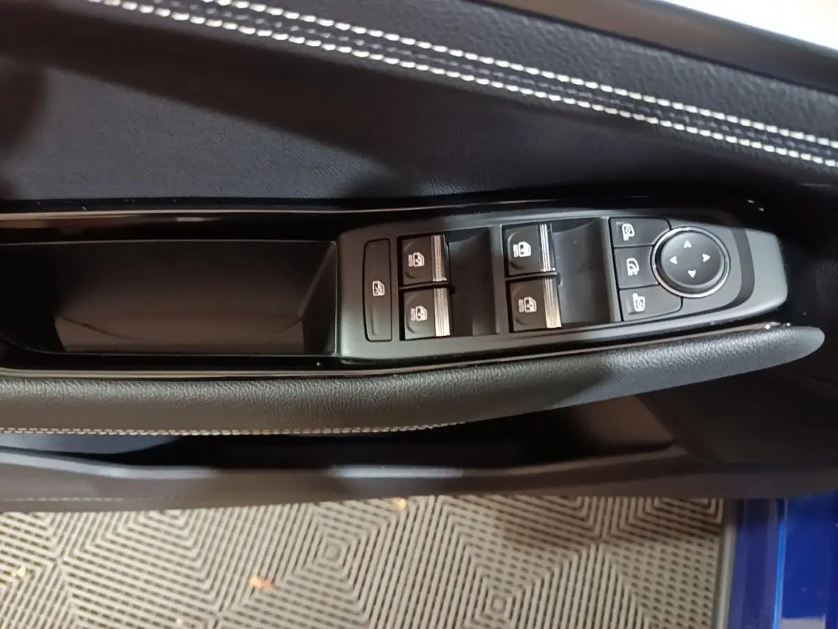Gros plan sur les commandes de lève-vitres et rétroviseurs sur la porte côté conducteur d’un Renault Austral bleu 2024.