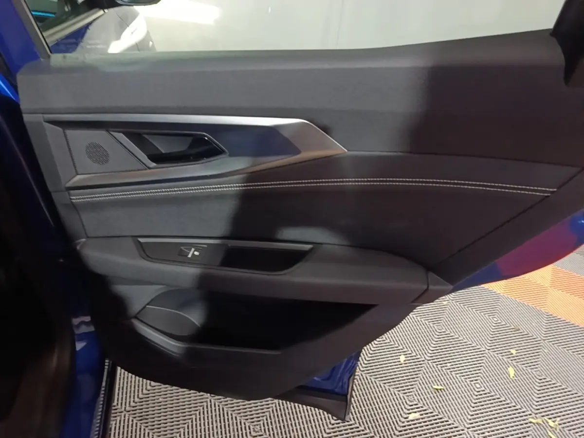 Vue intérieure de la porte avant gauche du Renault Austral 2024 bleu, avec garniture noire et surpiqûres blanches.