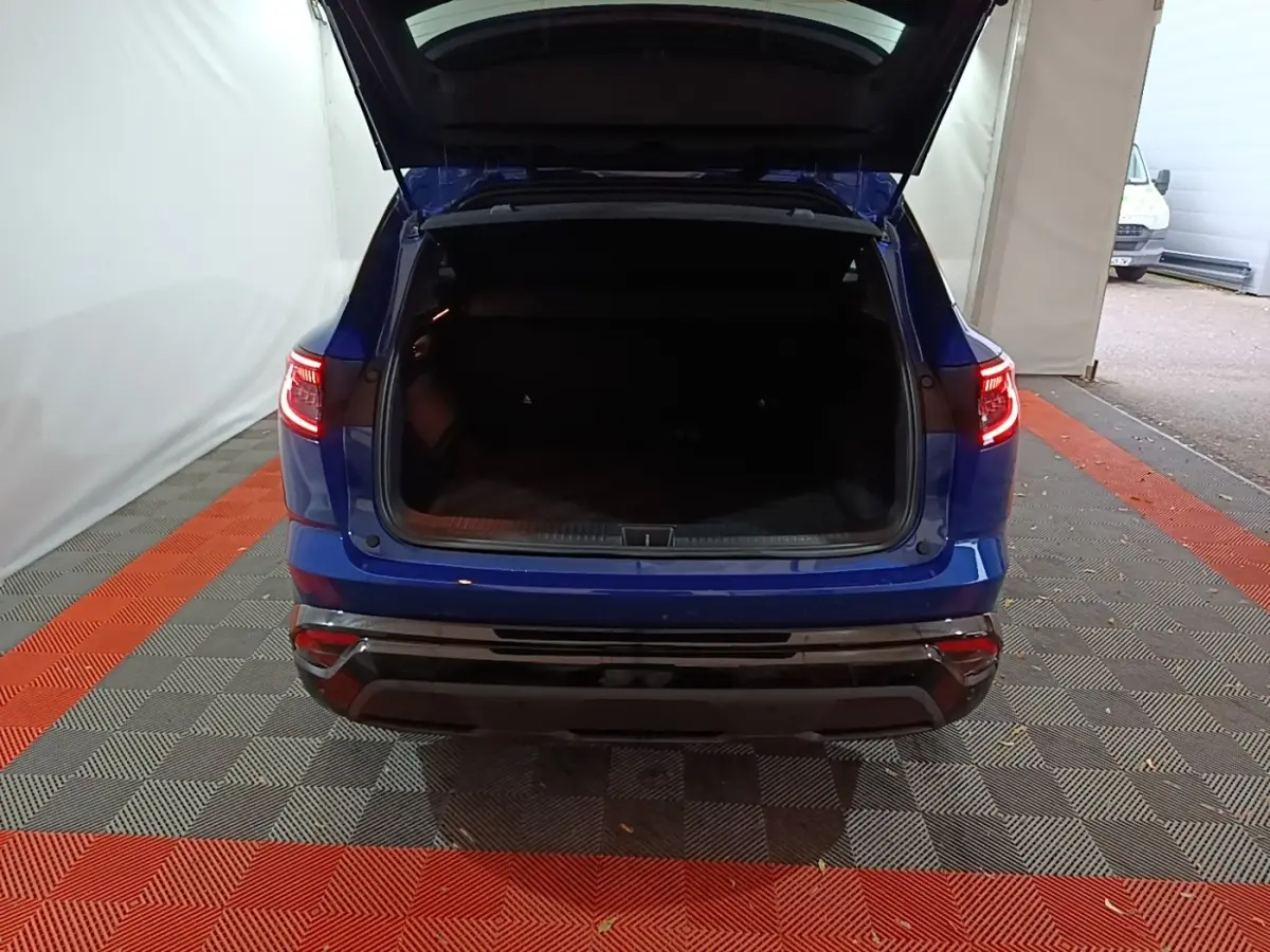 Vue arrière d'un Renault Austral bleu 2024 avec coffre ouvert et feux arrière allumés dans un garage.
