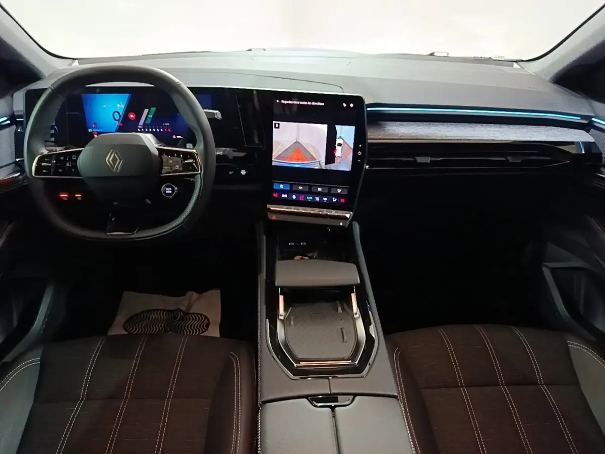 Intérieur Renault Austral 2024 vu de face, volant cuir multifonctions, écran tactile central vertical et éclairage d'ambiance bleu.