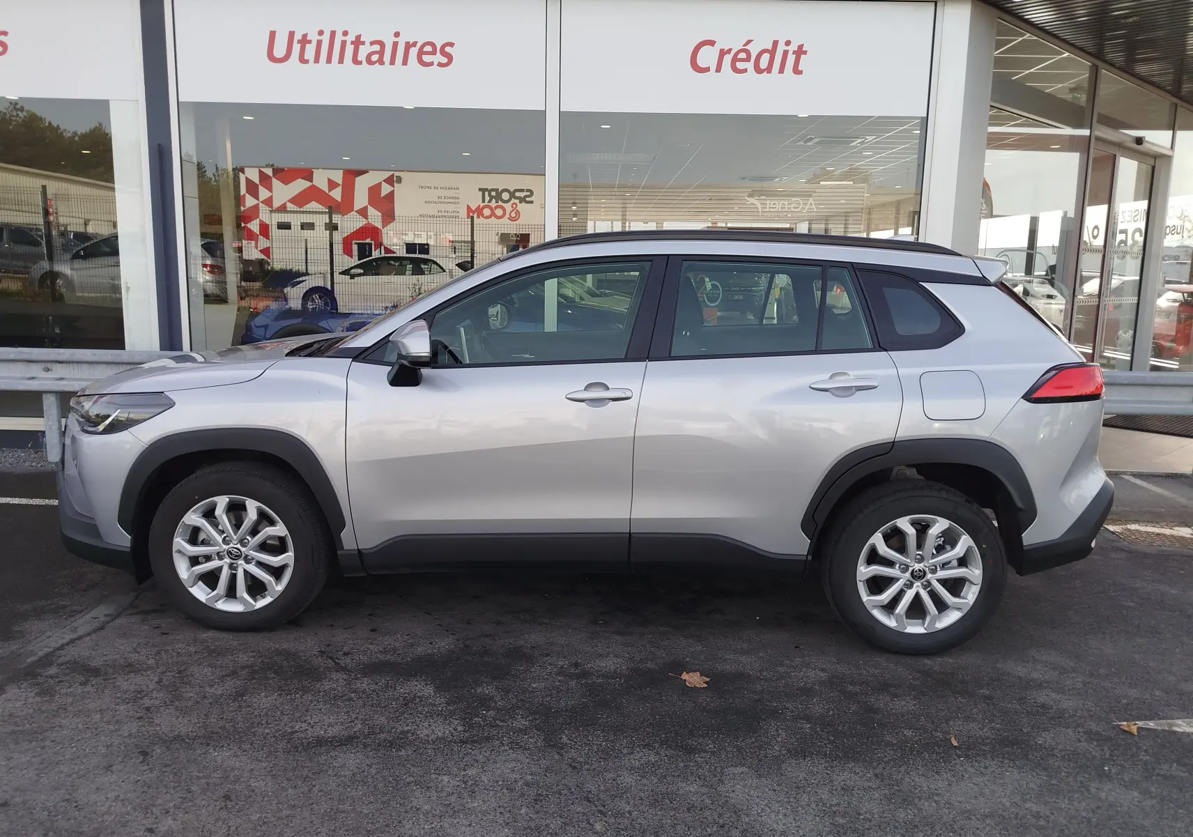 Profil côté gauche du Toyota Corolla Cross 1.8 Hybrid gris acier 2025, avec jantes alliage et protections noires sur les passages de roues.