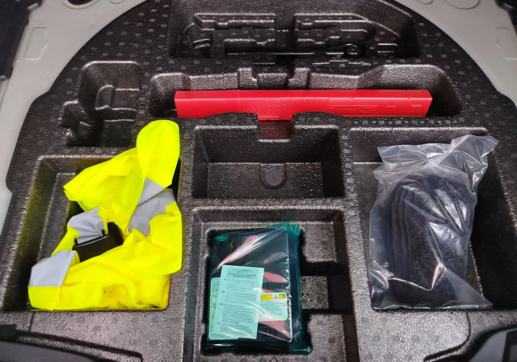 Rangement en mousse dans le coffre d'une Toyota Corolla Cross 2025 gris acier, contenant gilet jaune, triangle et accessoires d'urgence.