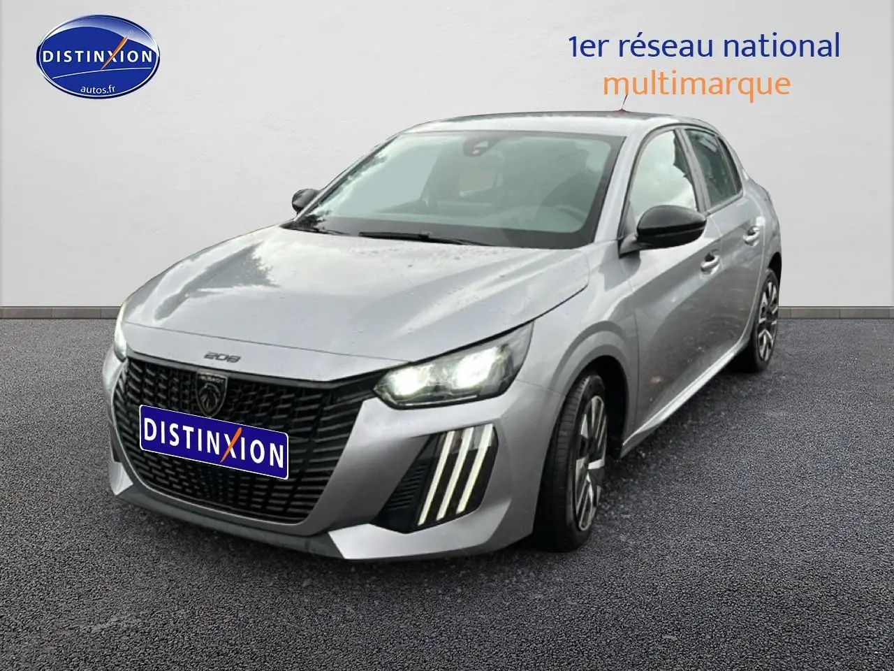 PEUGEOT 208 gris artense en 3/4 avant droit, avec phares allumés et feux diurnes à LED verticaux visibles.