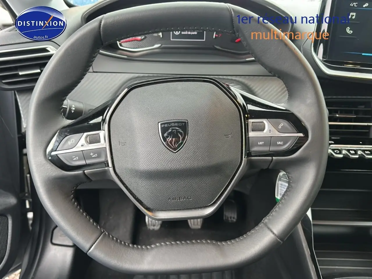 Vue rapprochée du volant noir de la Peugeot 208 1.2 PureTech 100 Active avec commandes intégrées et tableau de bord gris.