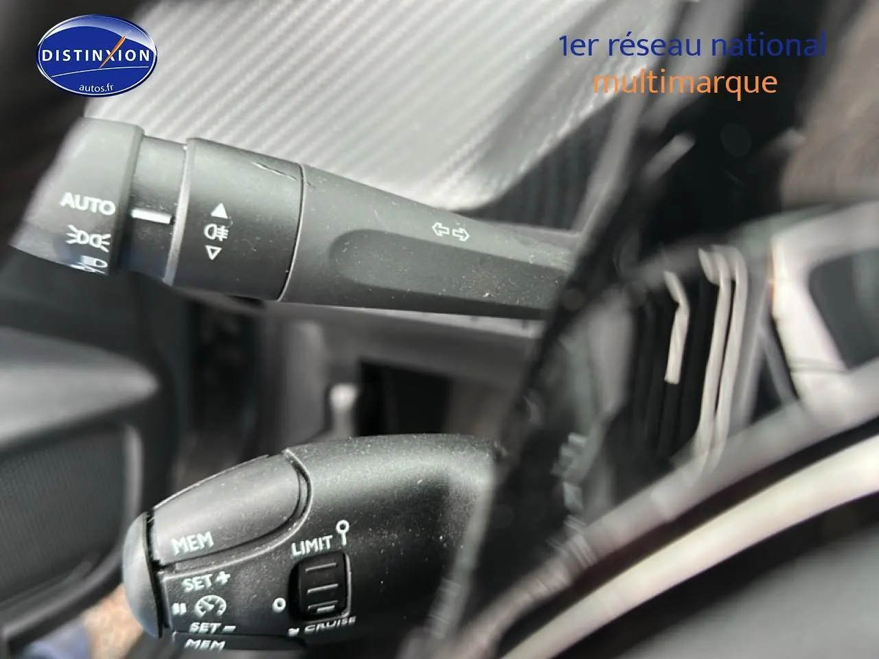 Détail du commodo gauche noir avec commandes de phares et régulateur sur Peugeot 208 gris Artense, intérieur proche.