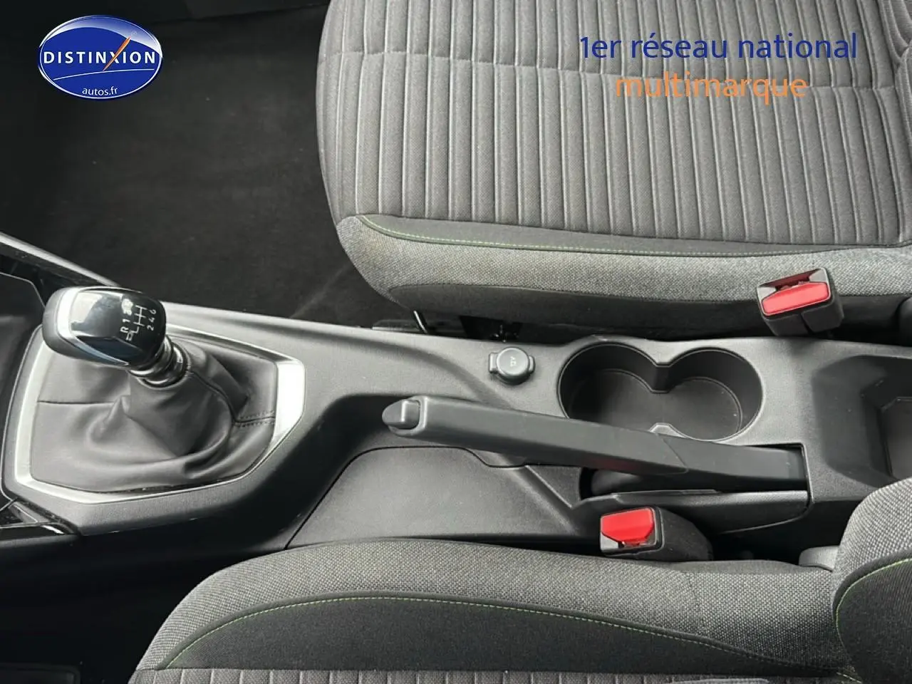 Vue intérieure centrée sur la console centrale d'une Peugeot 208 gris artense avec levier de vitesse manuel et sièges tissu noir/gris.