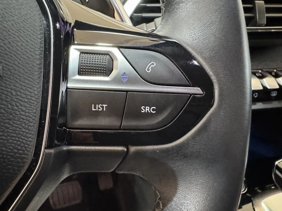 Gros plan sur les commandes gauche du volant noir du Peugeot 3008 orange, avec boutons téléphone et liste.