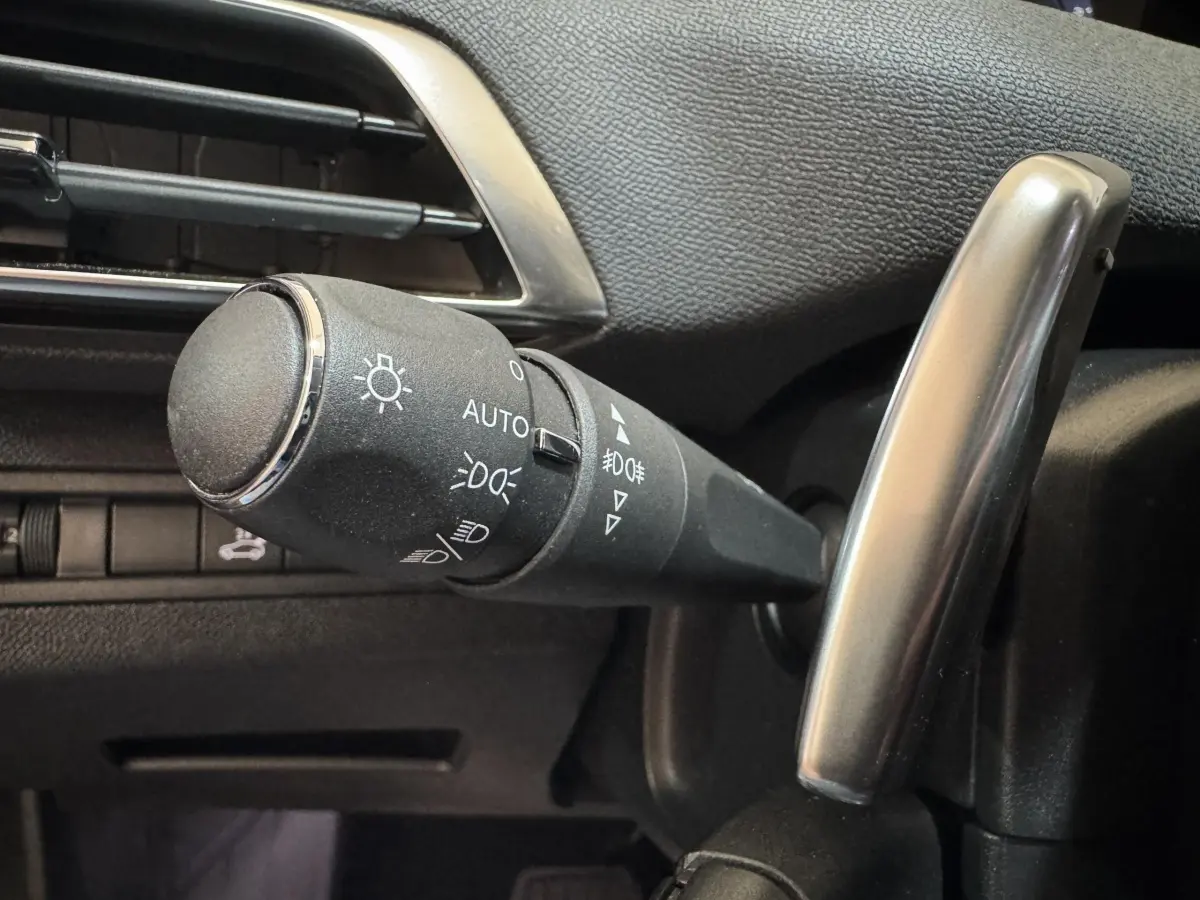 Gros plan sur la commande des phares à gauche du volant dans l’habitacle noir du Peugeot 3008 orange 2020.