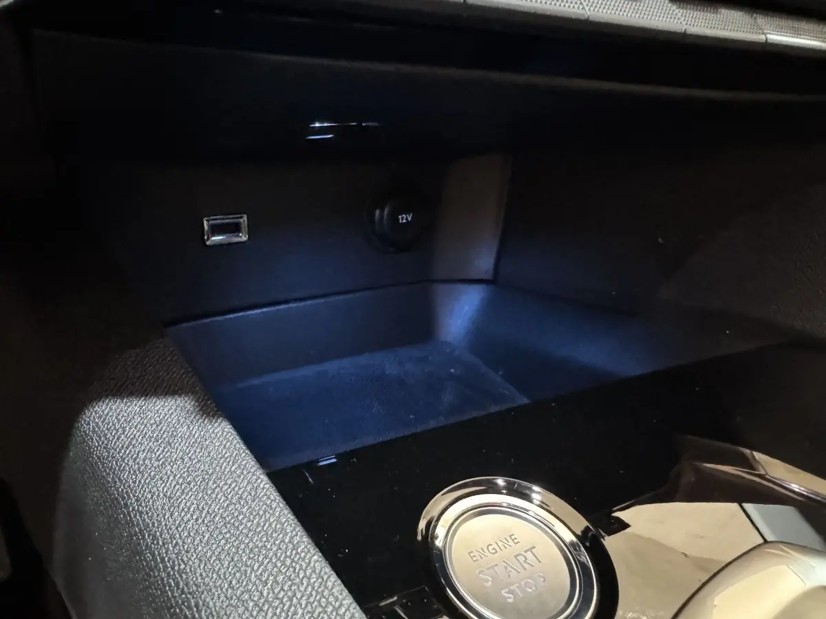 Détail intérieur du Peugeot 3008 PureTech 130, bouton démarrage/arrêt moteur et prise 12V sur console noire.