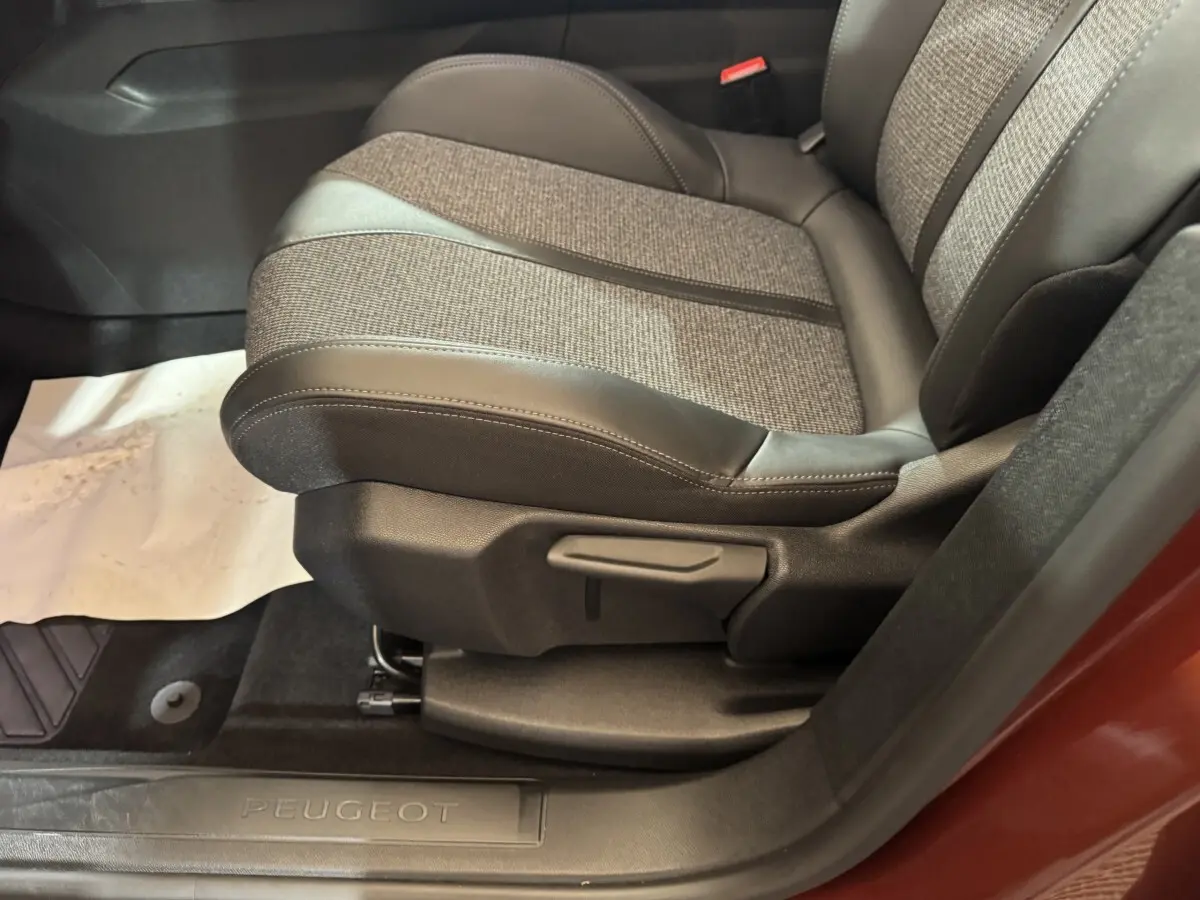 Gros plan sur le siège avant droit tissu et cuir gris d’un Peugeot 3008 orange, avec seuil de porte marqué Peugeot.