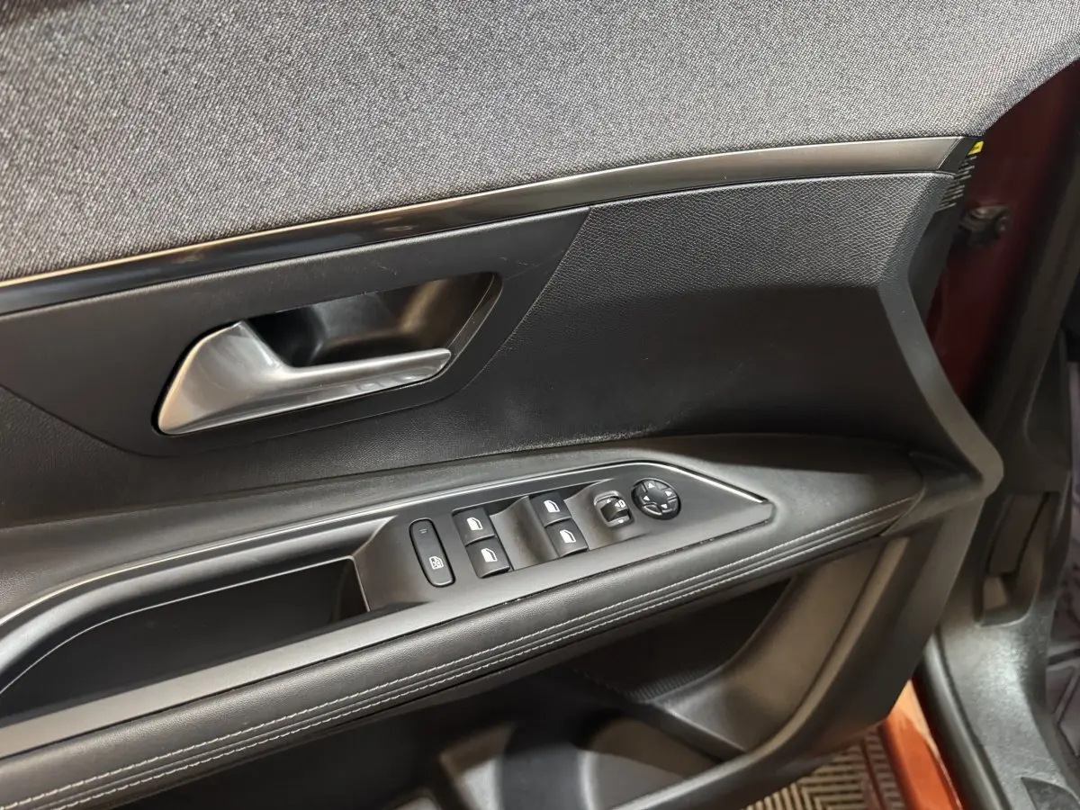 Vue rapprochée de la porte avant gauche de la Peugeot 3008 orange, montrant les commandes des vitres et le bouton de verrouillage.