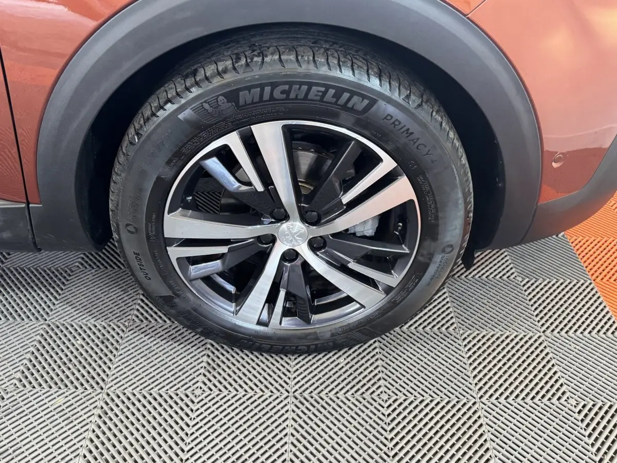 Gros plan sur la roue avant droite du Peugeot 3008 orange, avec jante alliage bicolore et pneu Michelin.