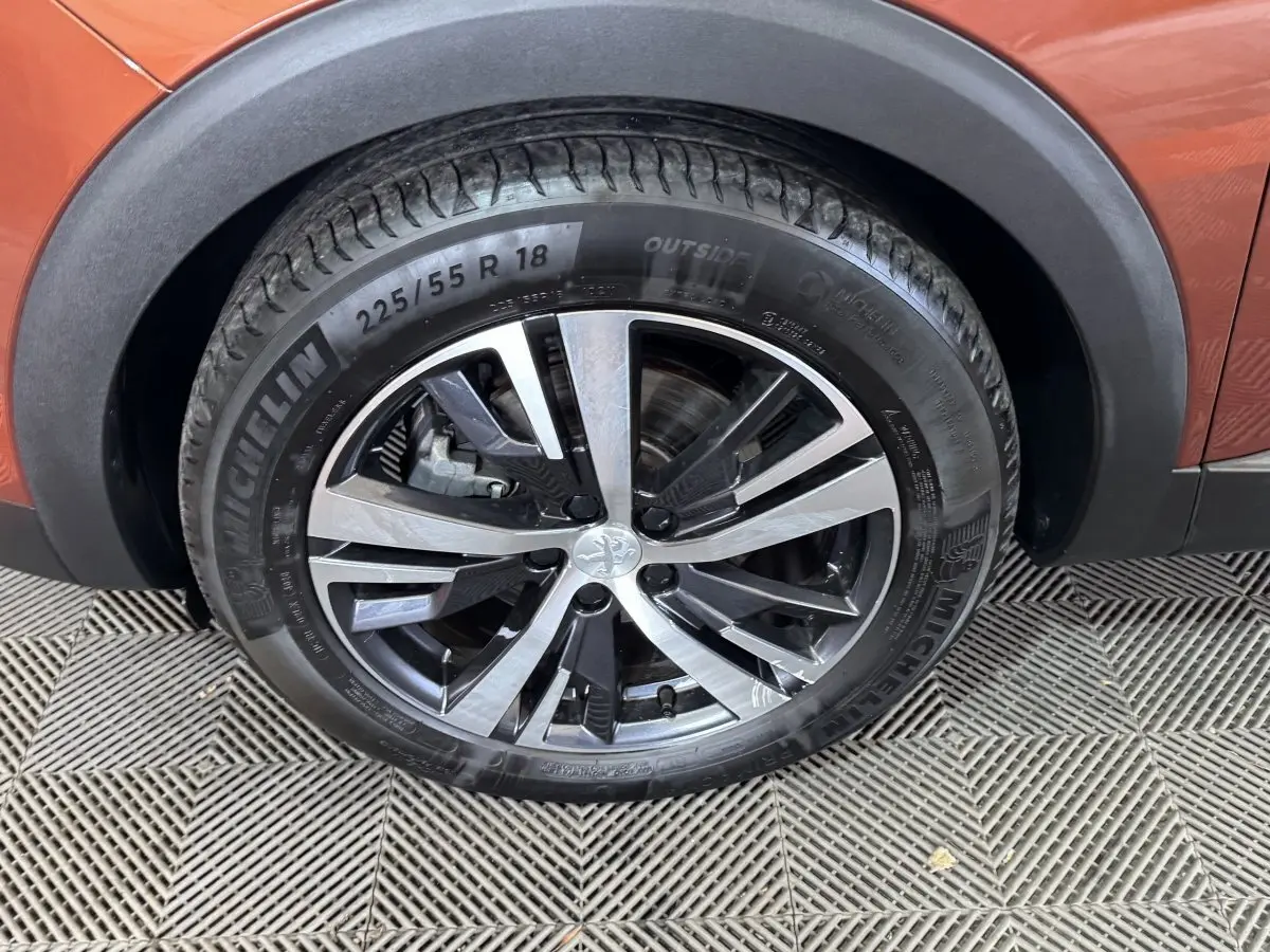 Gros plan sur la roue avant droite du Peugeot 3008 orange, mettant en valeur la jante alliage bicolore et le pneu Michelin.
