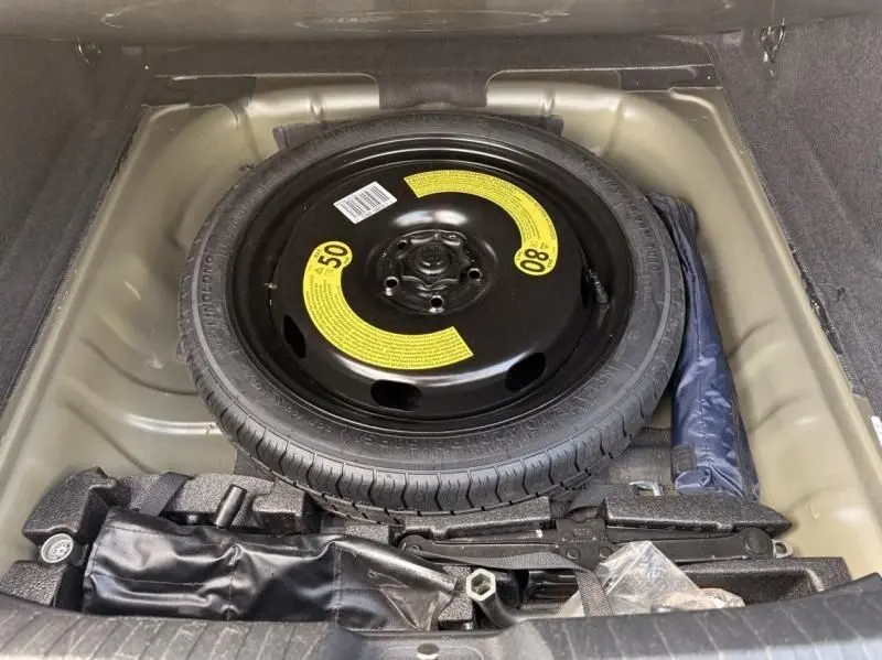 Vue plongeante sur la roue de secours compacte noire avec étiquettes jaunes dans le coffre d'une Audi A3 Berline gris foncé.