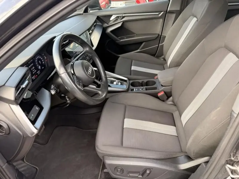 Vue intérieure côté conducteur de l'Audi A3 Berline 35 TFSI 2022, sièges tissu gris avec bande claire et volant multifonction.