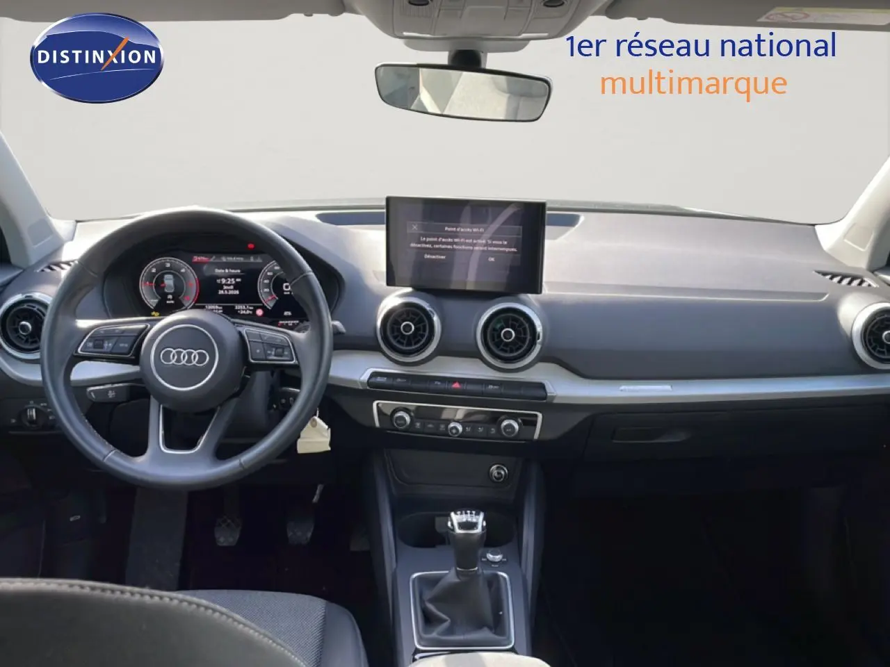 Vue intérieure avant de l'Audi Q2 30 TDI S-Line 2025, tableau de bord gris avec volant cuir et boîte manuelle.