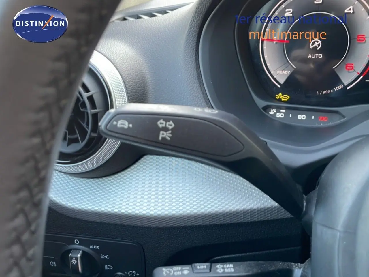 Gros plan sur la commande de clignotant à gauche du volant d’un Audi Q2 gris Manhattan, tableau de bord numérique visible.