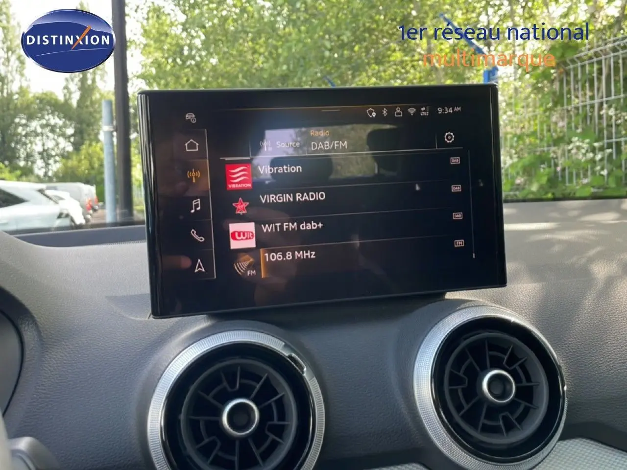 Écran central tactile de l'Audi Q2 30 TDI S-Line 2025, affichant les stations radio, avec aérateurs ronds en dessous.