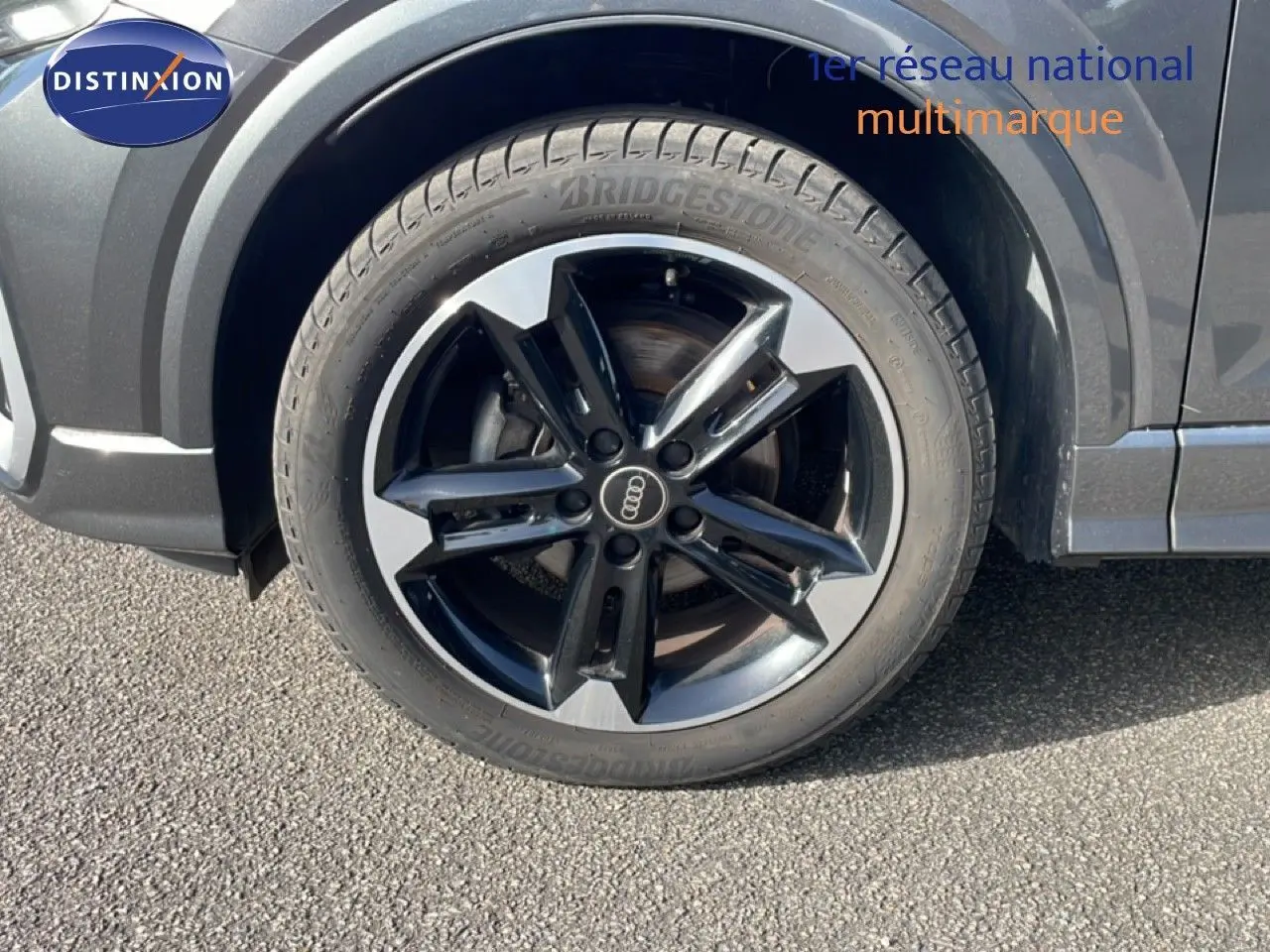 Gros plan sur la roue avant droite d’un Audi Q2 gris Manhattan avec jante alliage bicolore distinctive.