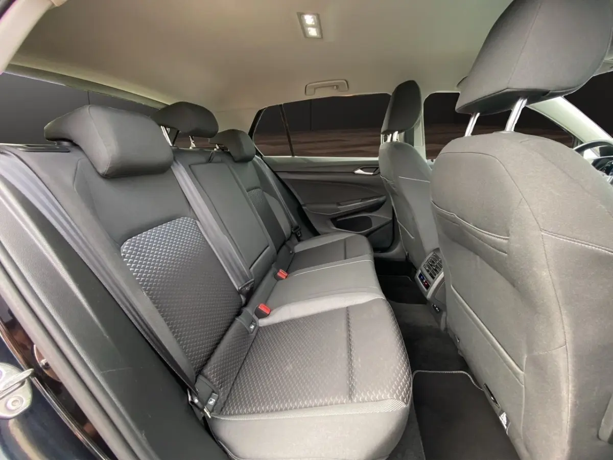 Vue intérieure arrière côté gauche de la Volkswagen Golf noire, montrant la banquette et les sièges avant en tissu gris.