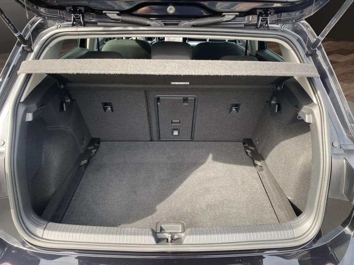 Coffre ouvert vu de l'arrière d'une Volkswagen Golf noire, montrant l'espace de chargement et la tablette cache-bagages.