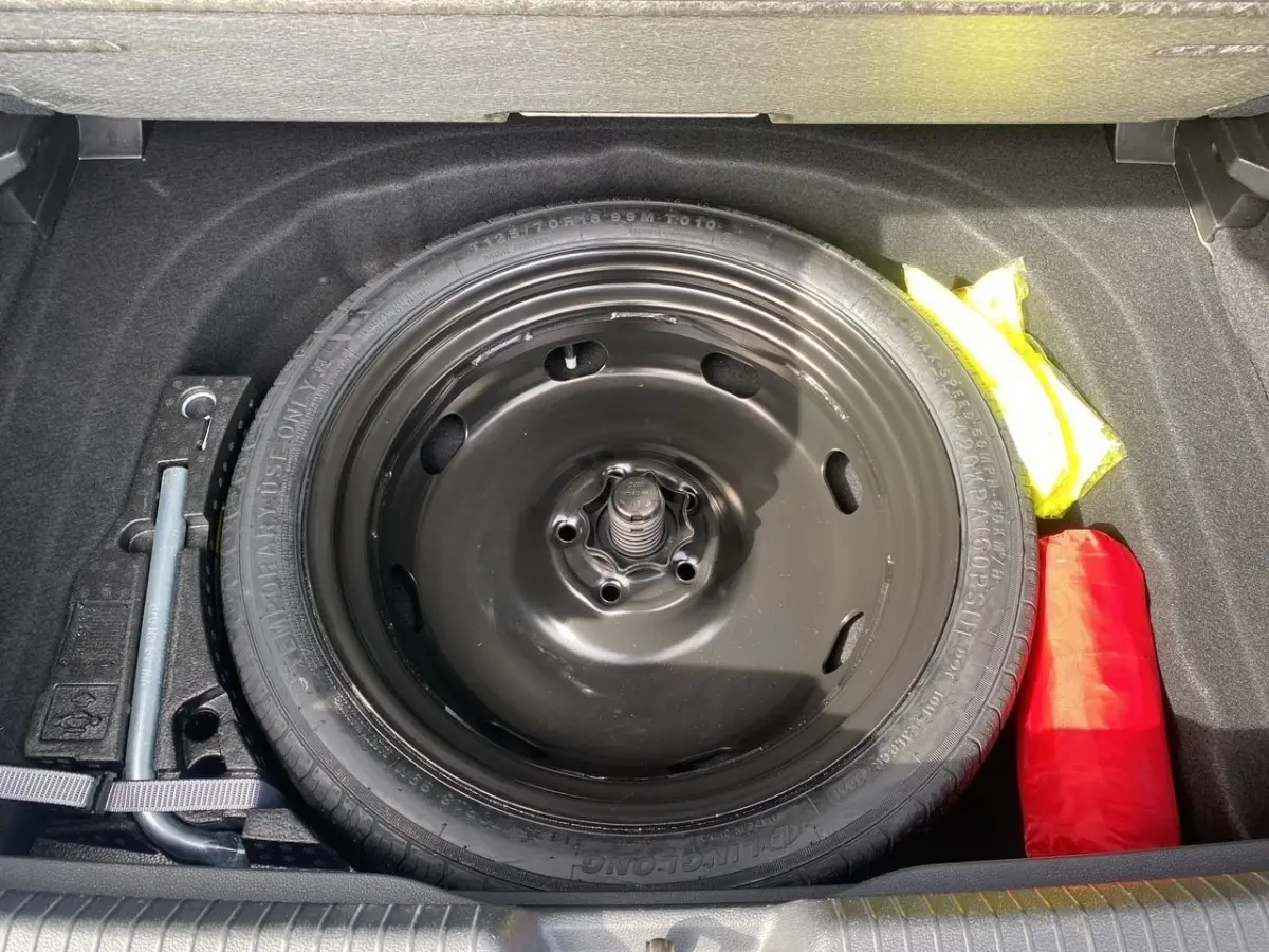 Vue plongeante sur la roue de secours noire et les accessoires de sécurité dans le coffre d'une Volkswagen Golf noire 2022.