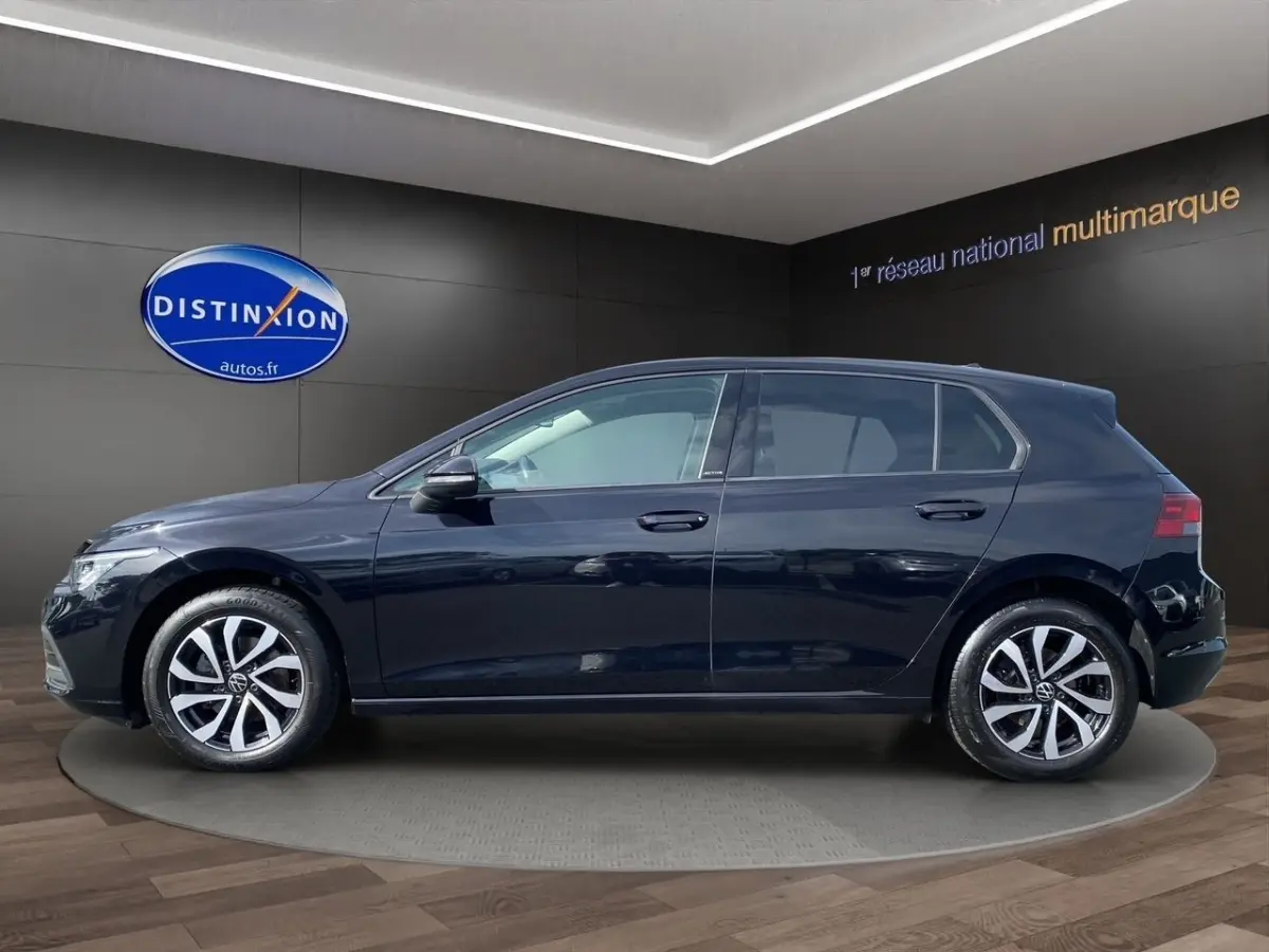 Profil côté gauche d'une Volkswagen Golf noire 2022 avec vitres surteintées dans un showroom.