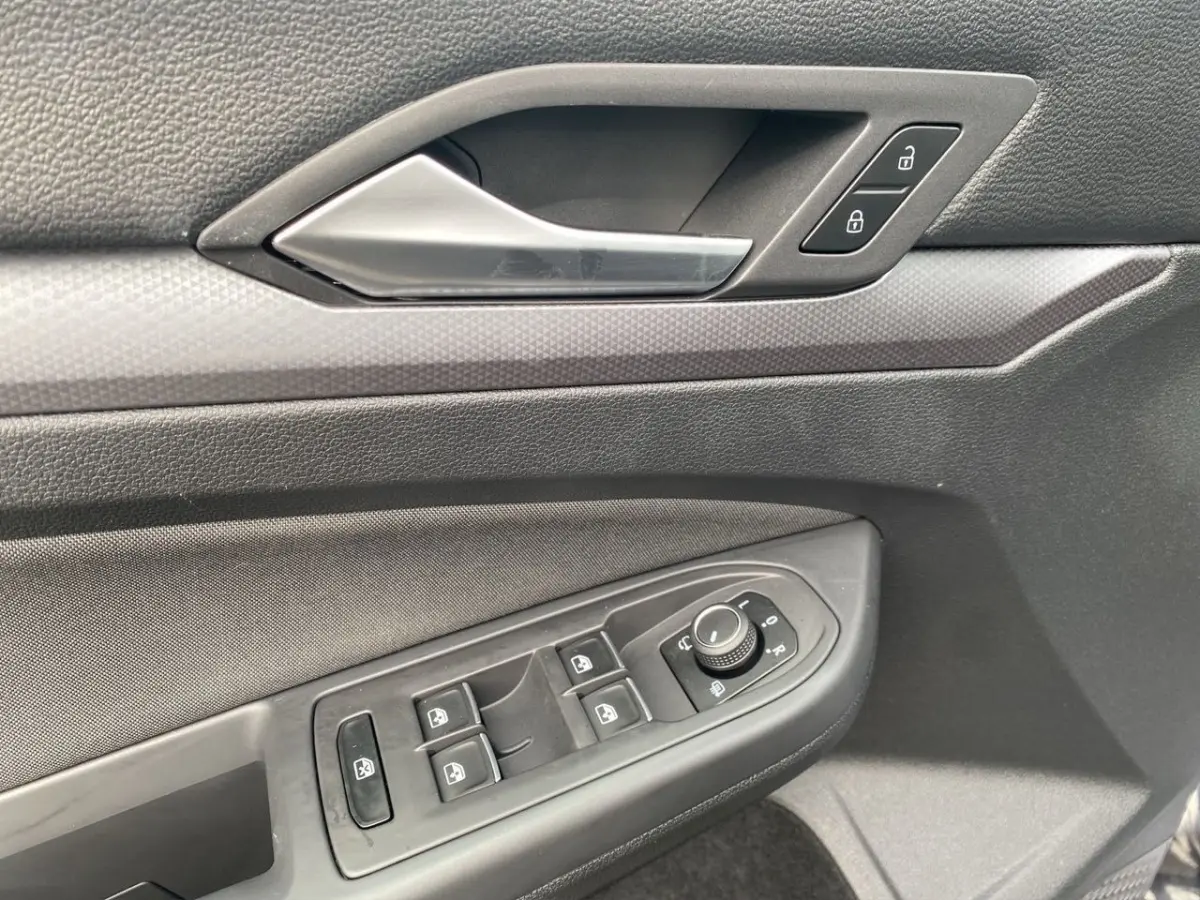 Gros plan sur la porte côté conducteur de la Volkswagen Golf noire, montrant la poignée et les commandes des vitres et rétroviseurs.
